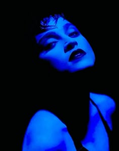 a woman with blue light on her face and chest in the dark, posing for a photo