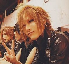 three people sitting next to each other in front of a wall and one person making the peace sign