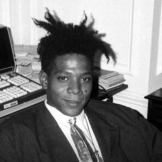 a young man wearing a suit and tie sitting in front of a desk with a computer