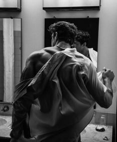 a man standing in front of a bathroom mirror with his back turned to the camera