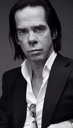 a man with long hair wearing a black suit and white shirt is posing for the camera