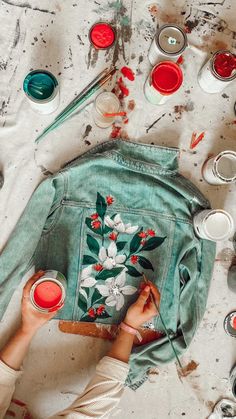 someone is painting on a jean jacket with red and white flowers in the center, surrounded by other paintbrushes