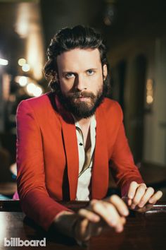 a bearded man sitting at a table with his arms crossed and looking off to the side