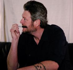 a man with a pen in his mouth sitting on a couch and looking off to the side