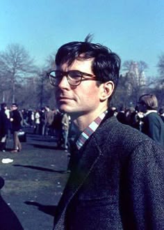 a man wearing glasses standing in the middle of a crowd