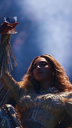 a woman holding a wine glass in her right hand and wearing a silver dress with sequins on it