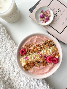 a bowl filled with fruit and nuts next to a book on a white tablecloth