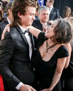 a man in a tuxedo hugging a woman on the red carpet