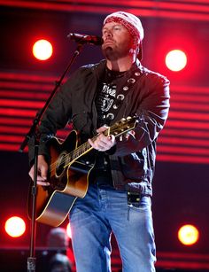 a man holding a guitar while standing in front of a microphone on top of a stage