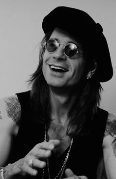 a black and white photo of a man with tattoos on his arm, wearing glasses and a hat