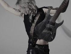 a woman holding an electric guitar in her right hand and posing for the camera with one arm outstretched