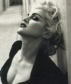 a black and white photo of a woman leaning against a wall with her eyes closed