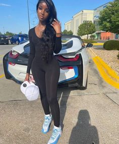 a woman standing in front of a car with her hand on her hip and holding a cell phone