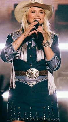 a woman wearing a cowboy hat and holding a microphone in front of her face while standing on stage