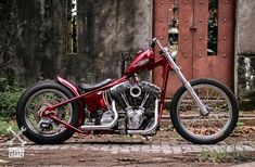 a red motorcycle is parked in front of a building with a door on the other side