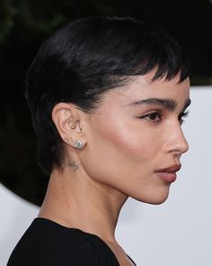 a close up of a person with short hair and piercings on her ear, wearing a black dress