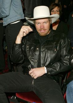 a man sitting in a chair wearing a white cowboy hat and black leather jacket with his hand on his hip